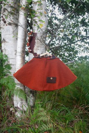 Capa de corte japonés para niños, amplia hasta la cadera de color rojo caldera. Con capucha de cuadros rojo caldera y marrón Botones de cascara de coco / madera Con un bolso plastón de lana.