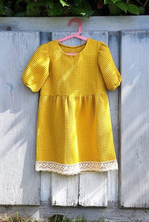 Vestido largo de corte japonés por la rodilla de relieves con cuadros amarillo con tela waffle, con manga abullonada hasta el codo y puntilla en el bajo. De algodón